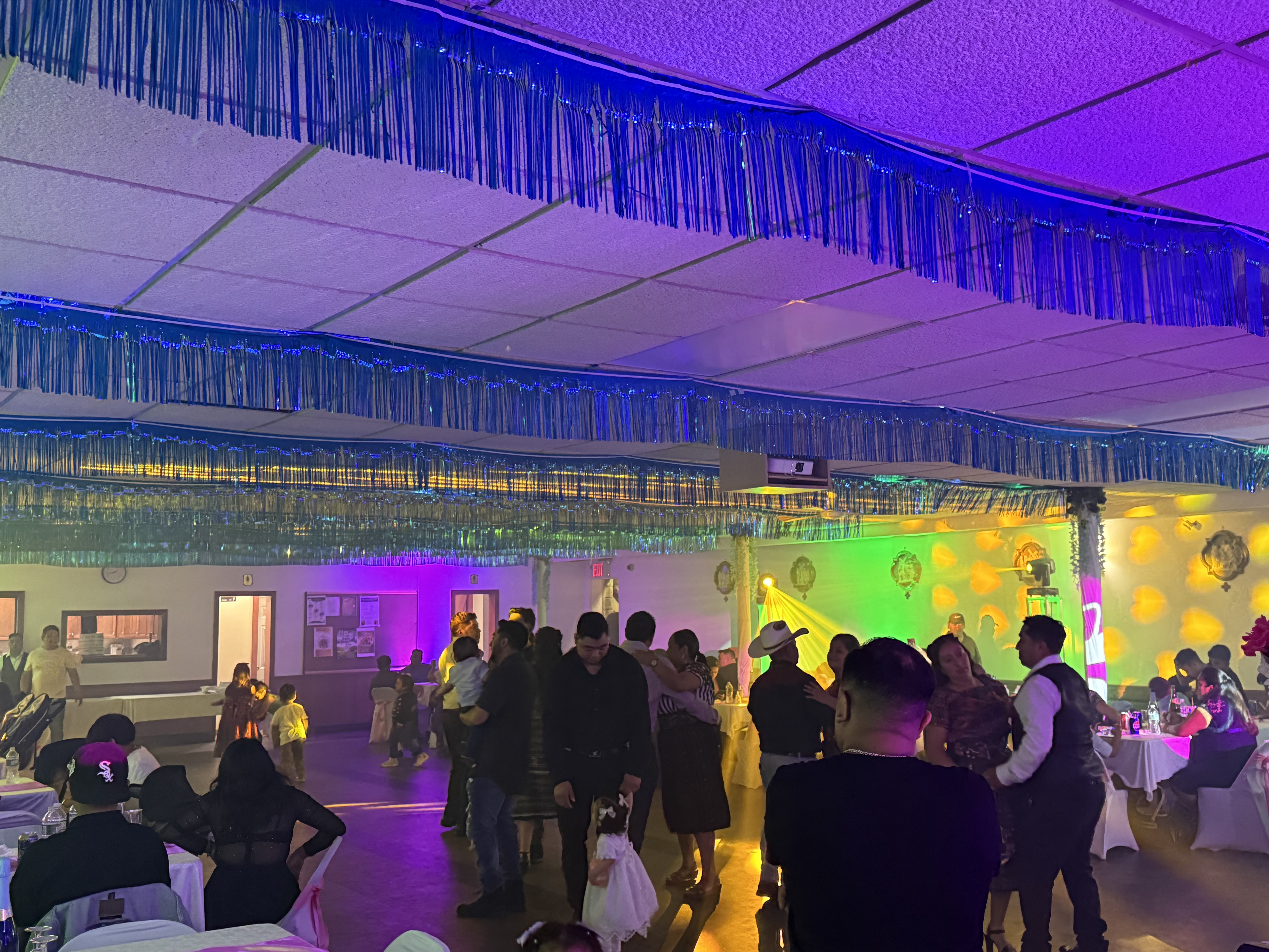 Pista de baile con luces púrpura, verdes y amarillas, invitados disfrutando la fiesta